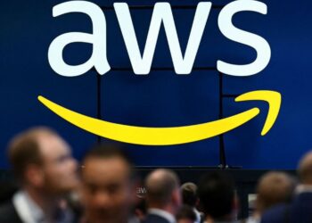 Logo de AWS en azul y blanco, con la flecha sonriente amarilla, sobre una multitud en el AWS re:Invent.