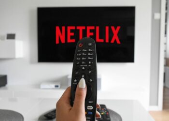 Mano sosteniendo control remoto apuntando a logo de Netflix en pantalla. Servicios de plataformas digitales de streaming afectados por la Reforma Fiscal Plataformas Digitales en México.