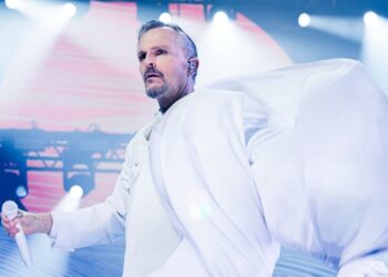 Miguel Bosé cantando en el escenario durante un concierto, iluminado por luces de espectáculo.