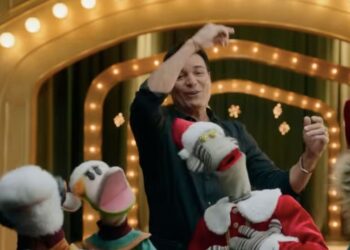 Chayanne posando junto a personajes de 31 Minutos en un escenario navideño lleno de luces y adornos.