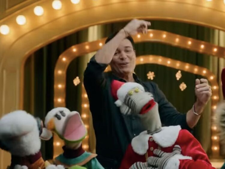 Chayanne posando junto a personajes de 31 Minutos en un escenario navideño lleno de luces y adornos.