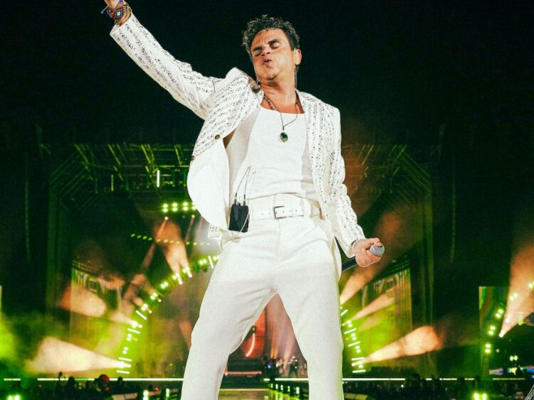 Silvestre Dangond cantando en un estadio lleno durante su gira internacional 2025, acompañado por luces de concierto y público celebrado.