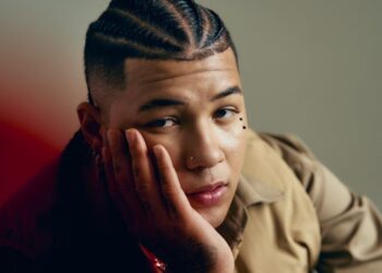 Retrato de Boza en escenario, micrófono en mano, durante la promoción internacional de “San Blas”, con luces y público de fondo.