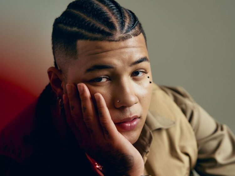 Retrato de Boza en escenario, micrófono en mano, durante la promoción internacional de “San Blas”, con luces y público de fondo.