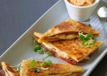 Sándwich bikini español de jamón y queso, caliente y crujiente, servido en un plato sencillo sobre una mesa rústica.