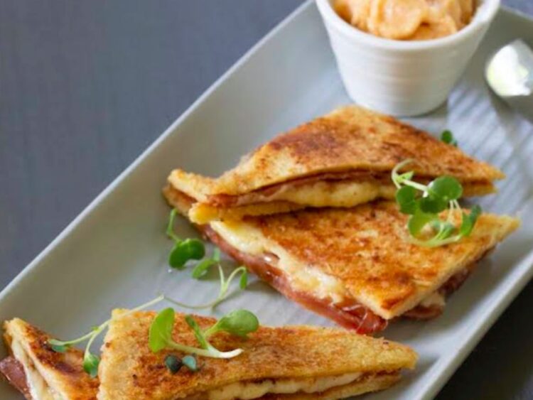 Sándwich bikini español de jamón y queso, caliente y crujiente, servido en un plato sencillo sobre una mesa rústica.