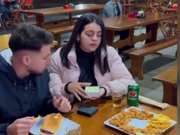 Una mujer muestra sorpresa al abrir un pequeño recipiente de mayonesa en un restaurante. La joven confundió el envase con una caja de anillo de compromiso, momento que se volvió tendencia en redes sociales. Foto: AMEXI/Redes Sociales.