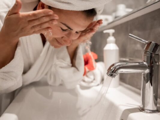Persona lava su rostro con agua en el lavabo como parte de su rutina diaria de cuidado facial.