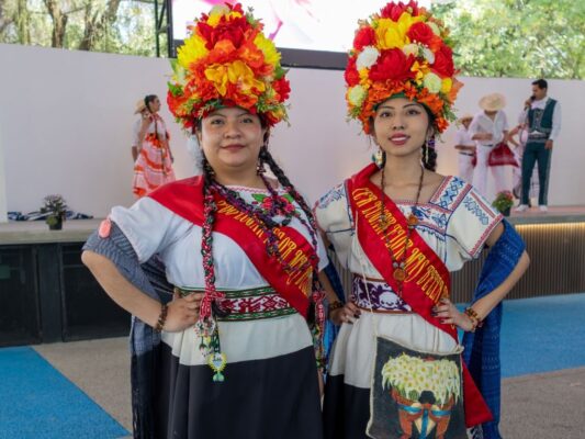 Jóvenes con atuendos tradicionales y tocados florales desfilan en el Centro Cultural Universitario de la UAM Xochimilco durante la Fiesta de la Flor Más Bella del Ejido.