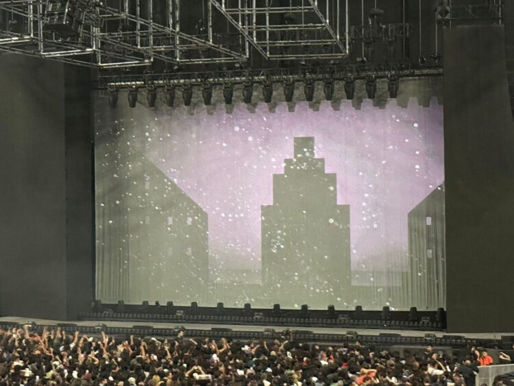 Miles de fanáticos esperan el inicio del concierto Soda Stereo ECOS en un foro de la Ciudad de México con la pantalla del escenario iluminada en azul.