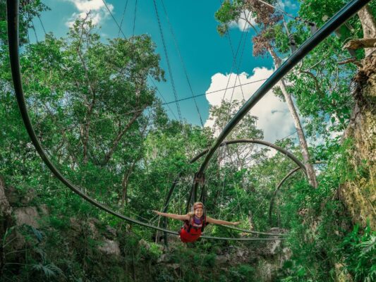 Personas disfrutan actividades en la Riviera Maya como tirolesas, ríos y recorridos en parques temáticos rodeados de selva.