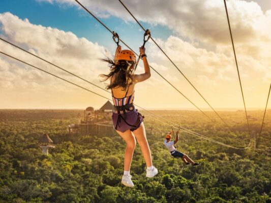 Personas disfrutan actividades en la Riviera Maya como tirolesas, ríos y recorridos en parques temáticos rodeados de selva.