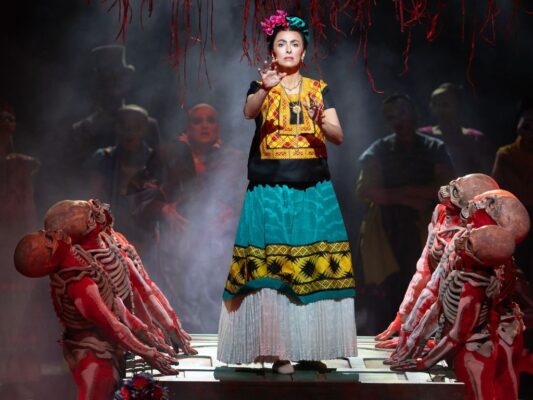 Escena de la ópera El último sueño de Frida y Diego con personajes inspirados en Frida Kahlo y Diego Rivera dentro de una escenografía surrealista.