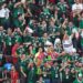 Aficionados mexicanos celebran durante un partido en una zona de reunión deportiva con banderas y camisetas de la selección.