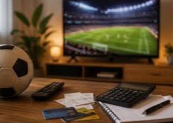 Escritorio con balón de futbol y pantalla al fondo transmitiendo un partido en televisión
