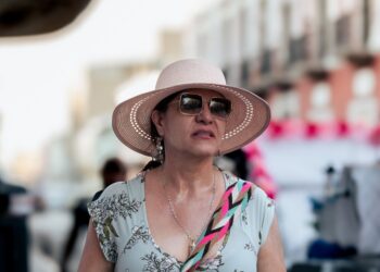 Persona con sombrero y lentes oscuros protege su rostro del sol durante un recorrido al aire libre.
