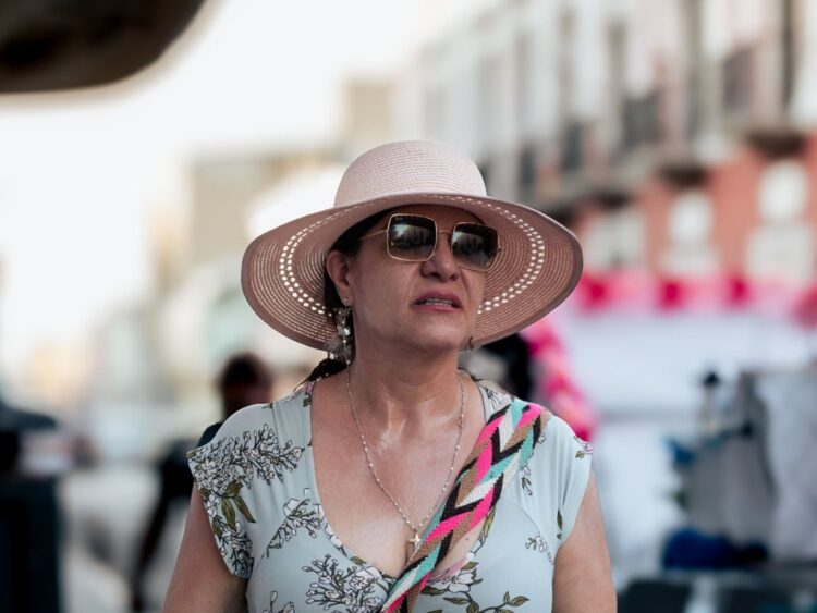 Persona con sombrero y lentes oscuros protege su rostro del sol durante un recorrido al aire libre.