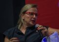Productora Inna Payán con gafas rojas hablando por micrófono durante una conferencia magistral en el Festival Internacional de Cine Guanajuato.