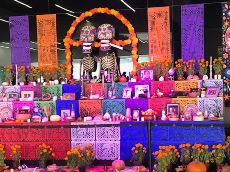 Altar tradicional de Día de Muertos decorado con flores de cempasúchil, veladoras, papel picado, pan de muerto, calaveras y fotografías de seres queridos.