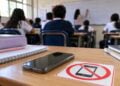 Regulación de celulares en escuelas: teléfono móvil sobre un pupitre con señal de uso restringido durante una clase.