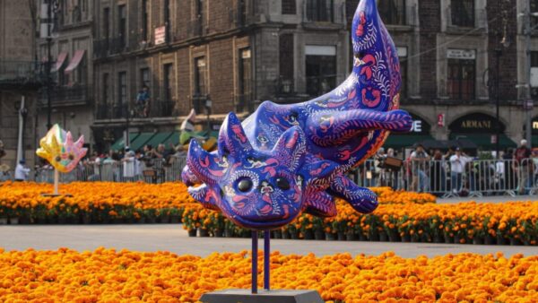 Escultura de ajolote azul decorada con diseños coloridos rodeada de flores de cempasúchil