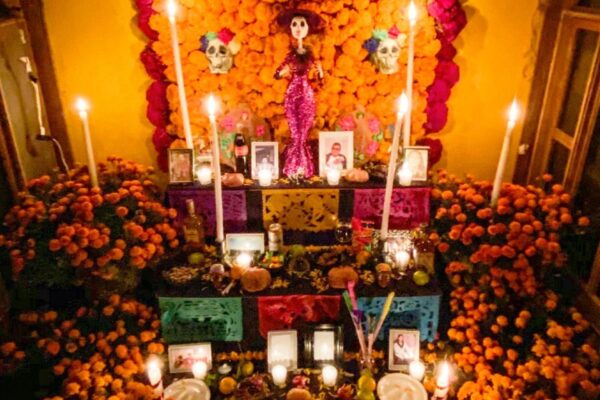 Ofrenda tradicional de Día de Muertos decorada con flores de cempasúchil, veladoras, papel picado, pan de muerto, alimentos y fotografías de seres queridos.
